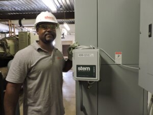 A man wearing a hard hat stands in front of a STEM power monitor.